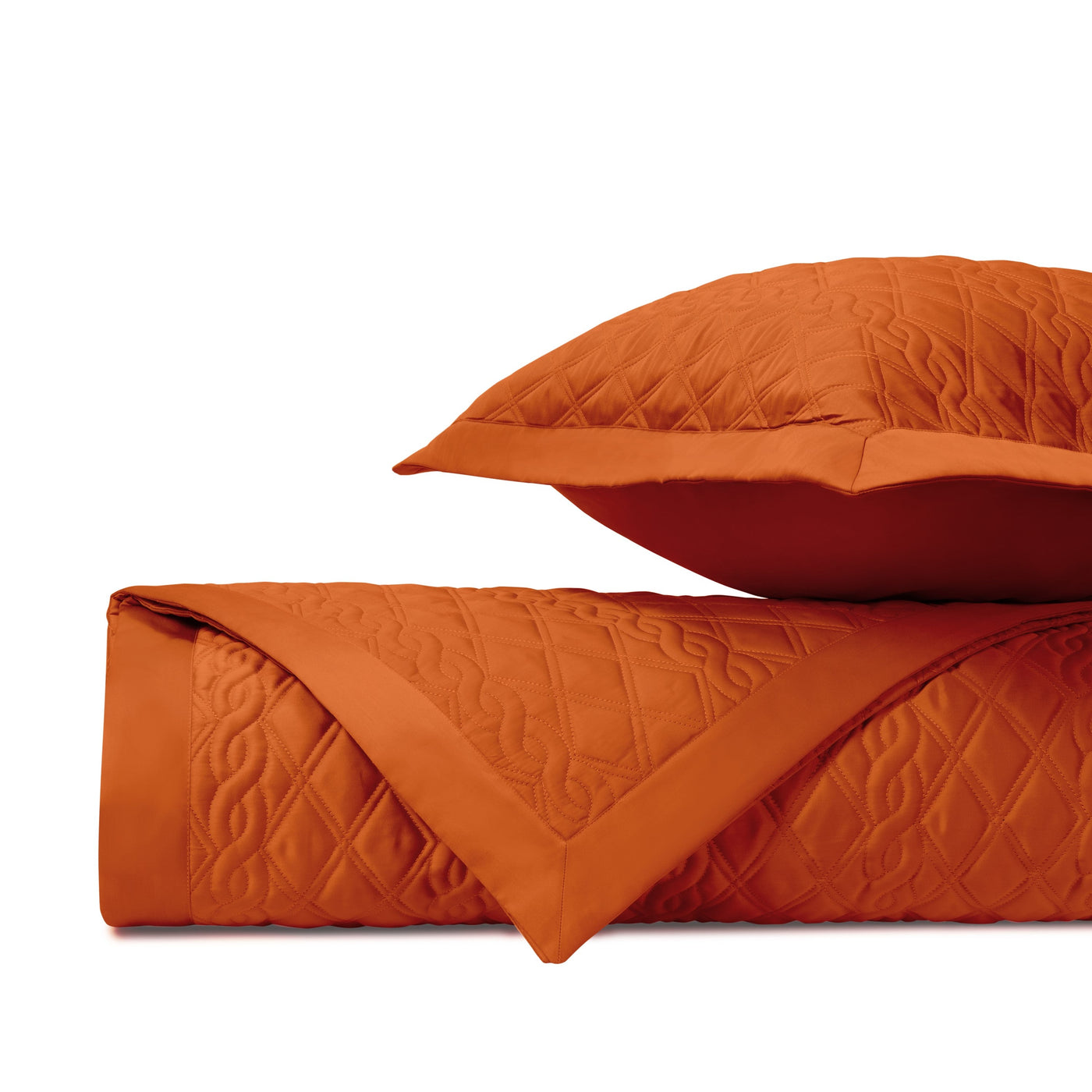 Folded tangerine quilted coverlet with diamond stitching beside matching sham.