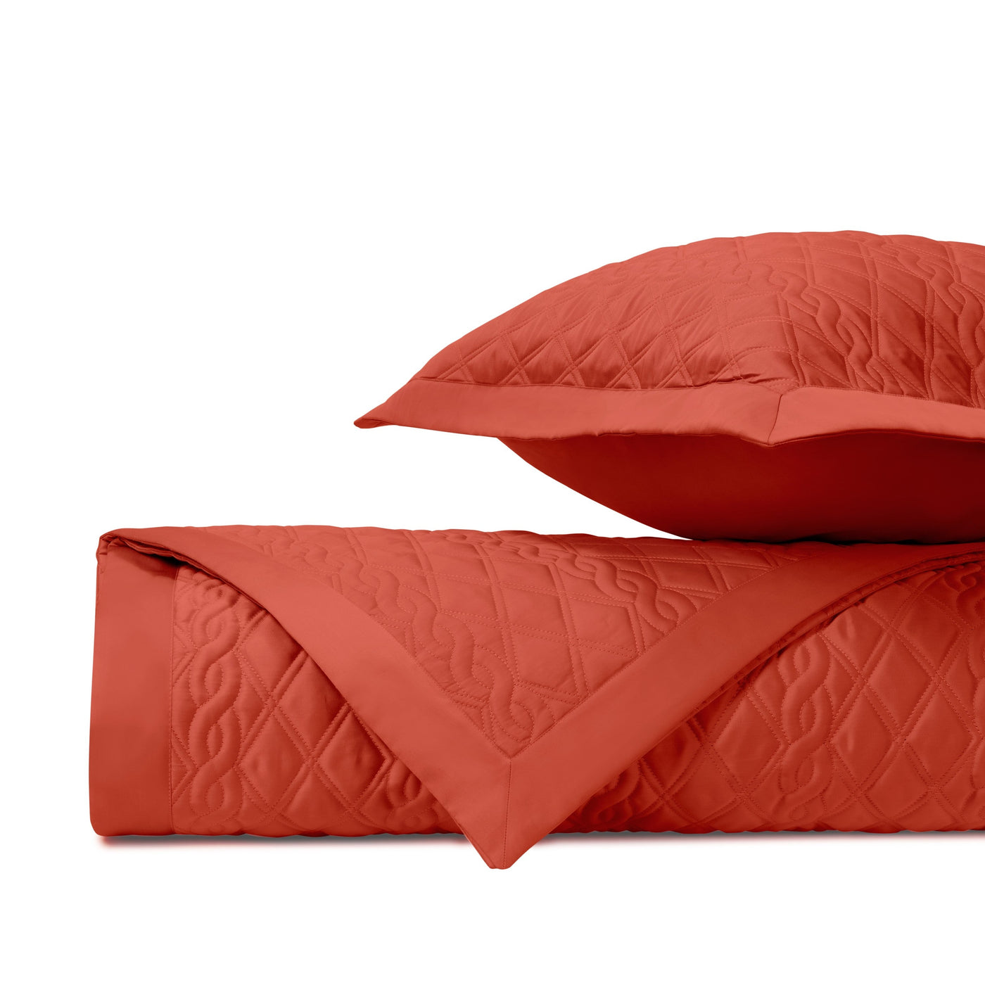 Folded coral quilted coverlet with diamond stitching and matching sham detail.