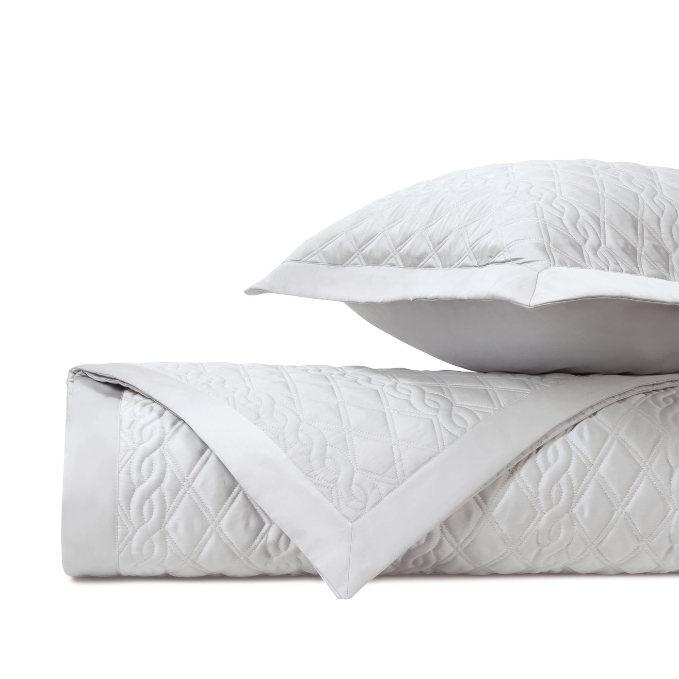 Folded white quilted yardage with geometric embroidered pattern and sham, white background.
