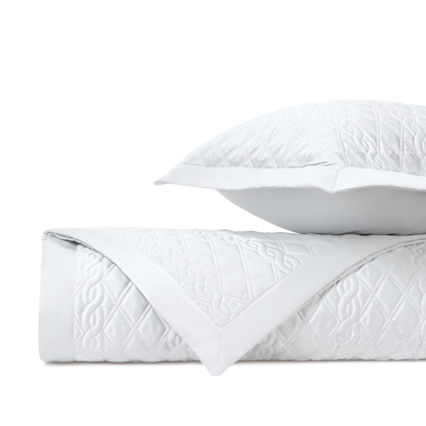 Folded white quilted fabric with diamond and scroll embroidered pattern, shown with matching sham.