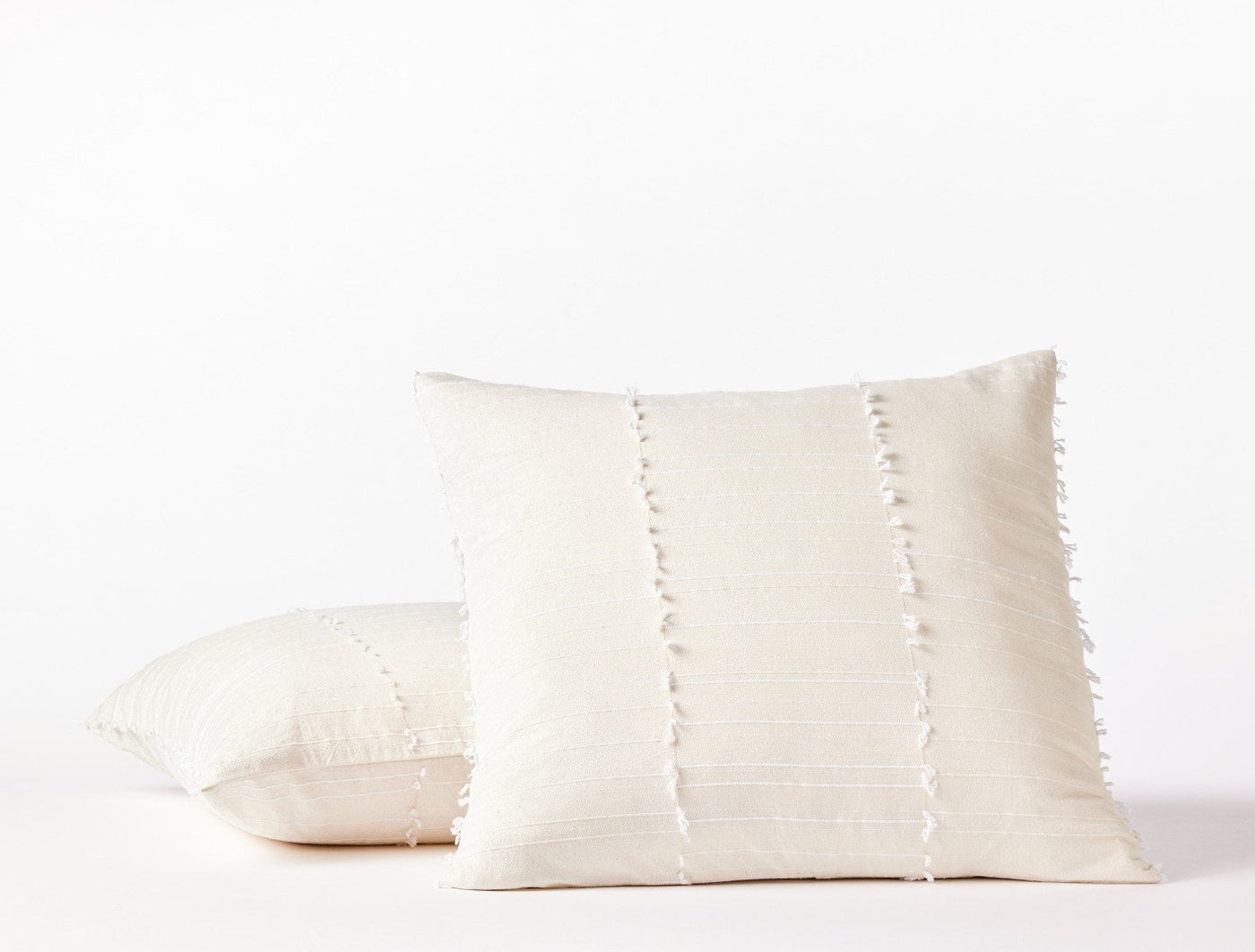 Two Coyuchi Precita ivory pillow covers stacked, showing fringe seam detail on textured linen.