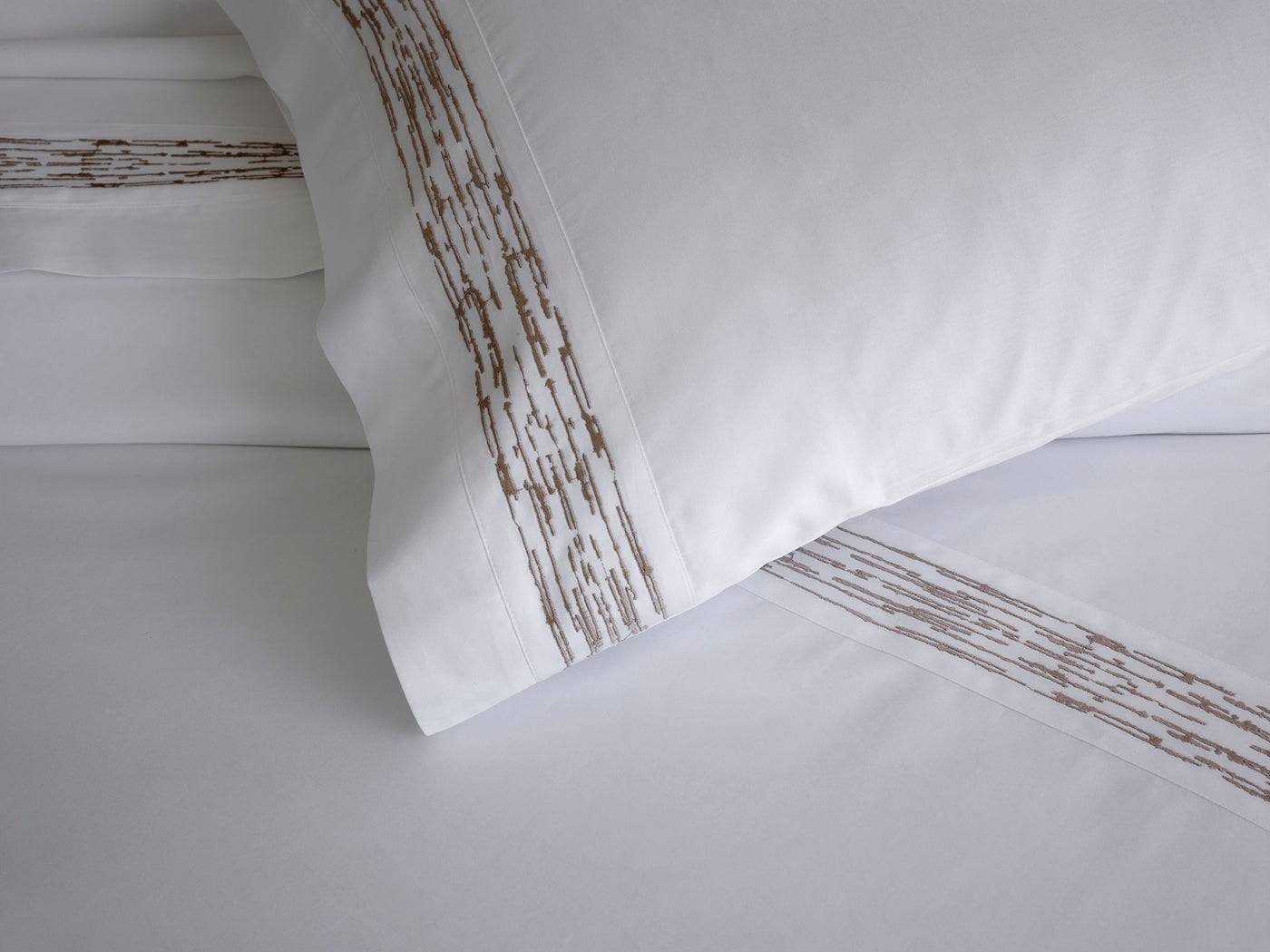 Close-up of taupe embroidered branch motif border on white cotton flat sheet.
