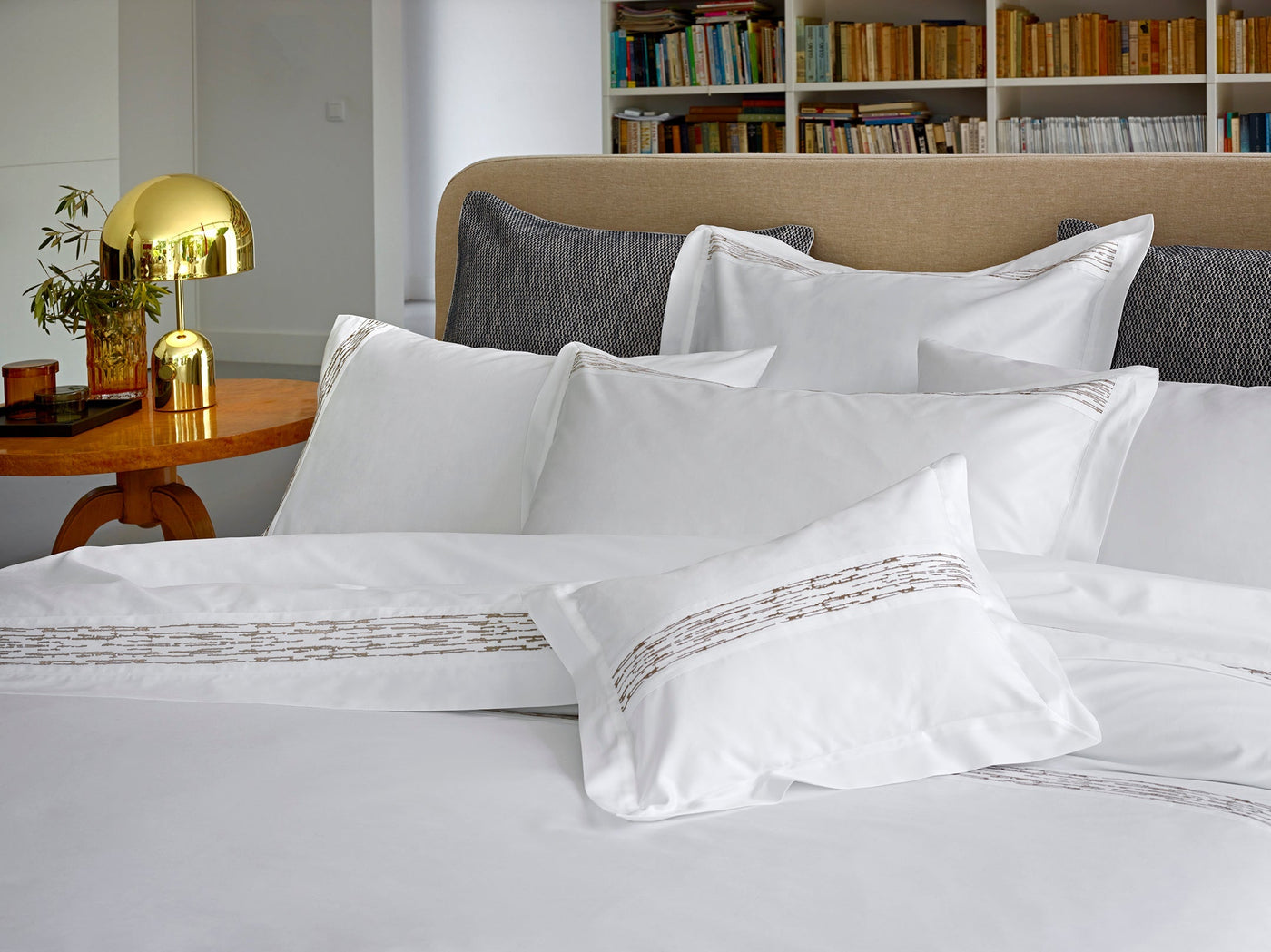 Close-up of Alentejo shams in white with taupe embroidered border detail layered on a made bed.