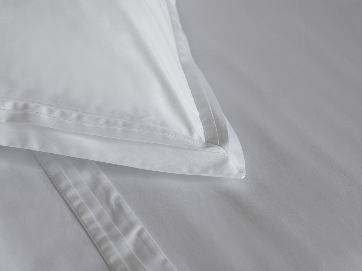 Close-up of white cotton pillow sham corner showing delicate woven stripe border detail.