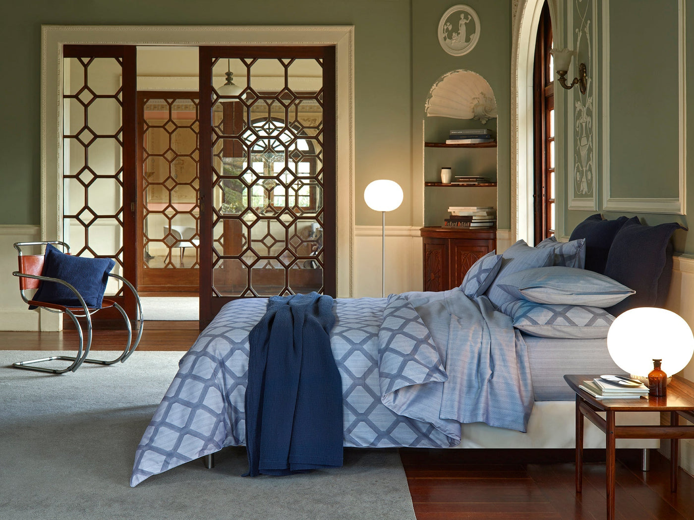 Blue geometric-patterned bedding styled in a sage green room with ornate wooden doors.