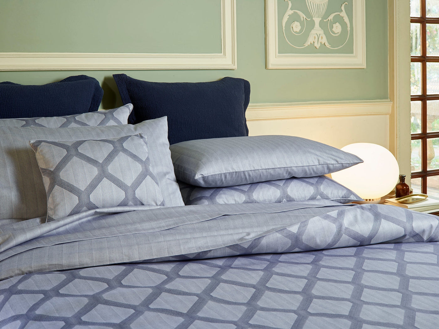 Periwinkle geometric jacquard shams styled with navy pillows on a made bed.