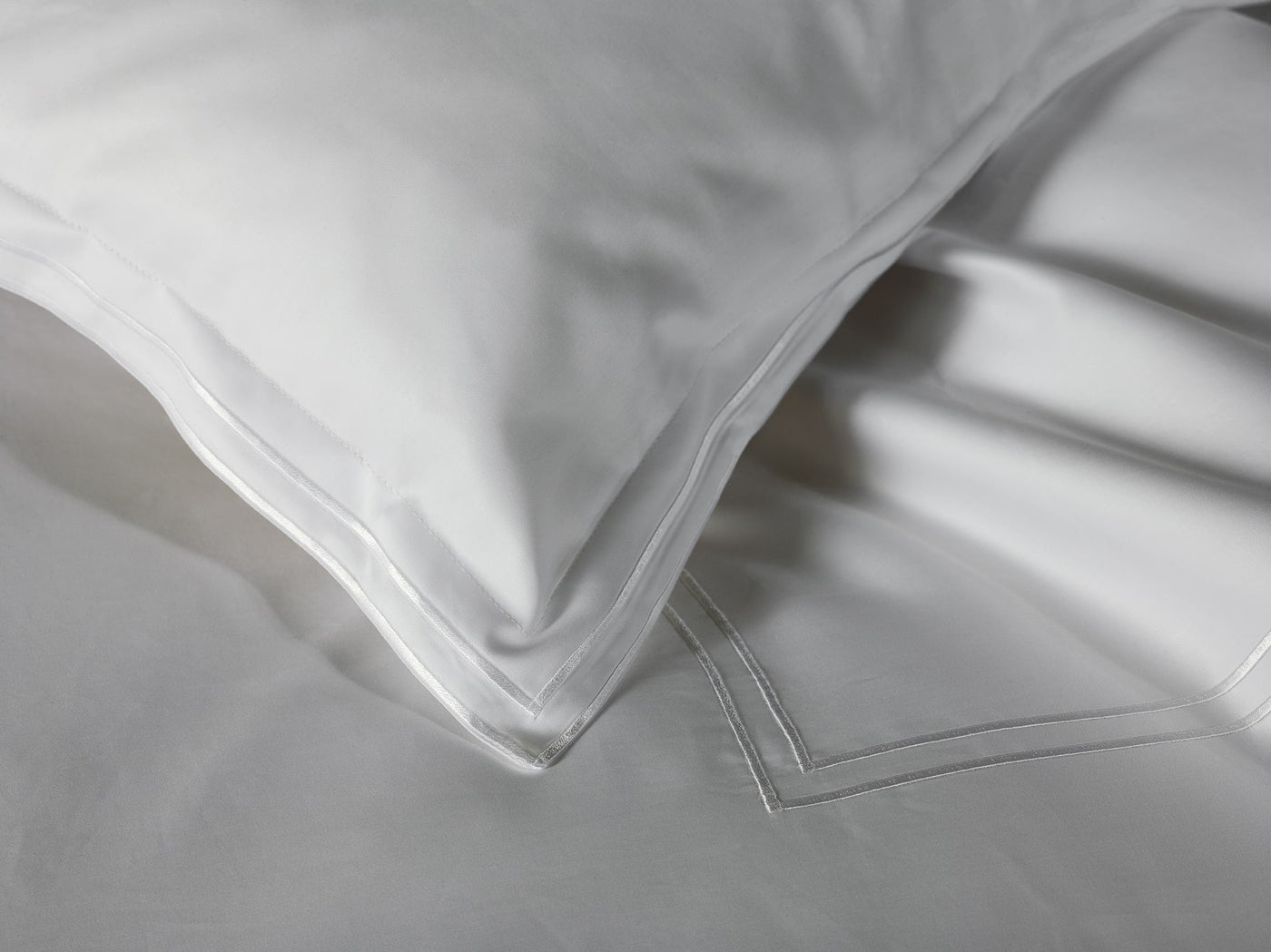 Close-up of Sferra's Sereno Fitted Sheet in white Egyptian cotton sateen, featuring a subtle stitched border, paired with a matching pillow.