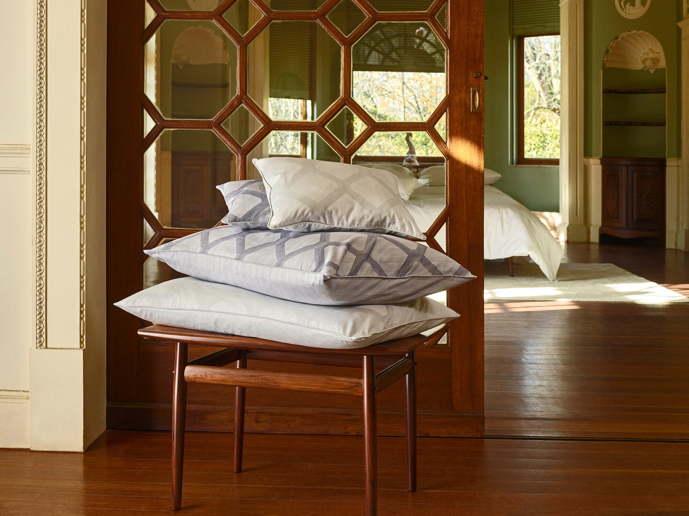 Stacked pale blue geometric-embroidered shams on a wooden stool before an ornate mirrored doorway.