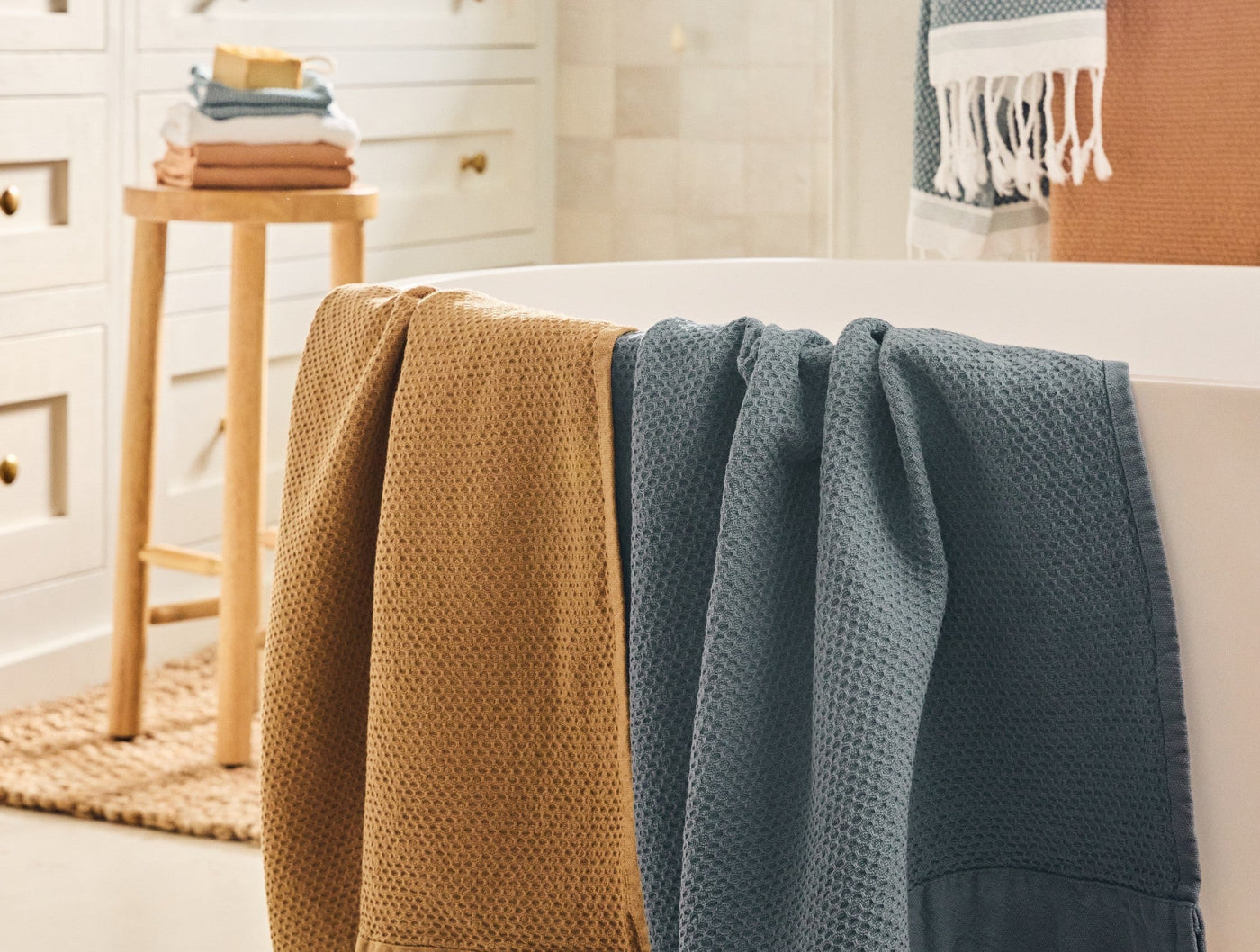 Saffron and slate waffle-weave guest towels draped over a white bathtub edge.