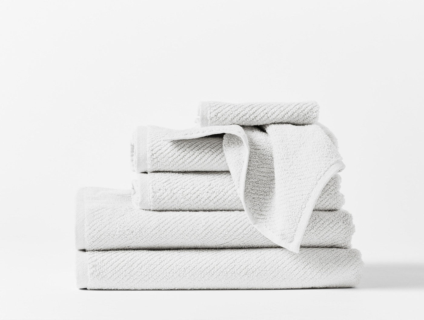 Coyuchi Air Weight wash cloth in white, stacked with matching towel set on white background.