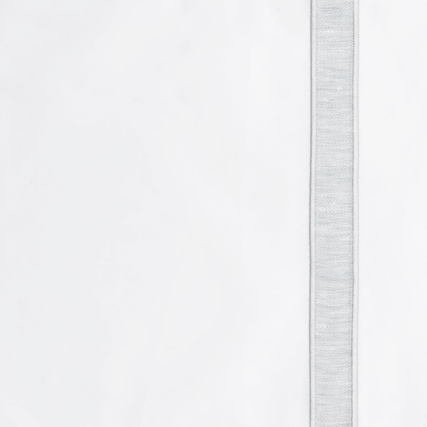 Close-up of silver woven border trim detail on white linen dinner napkin.