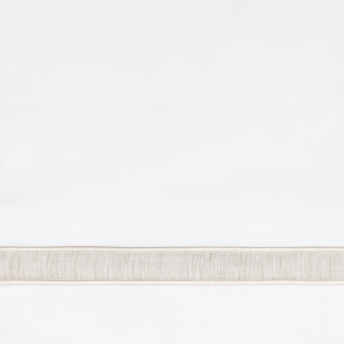 Close-up of woven linen border trim in natural ivory on white fabric.