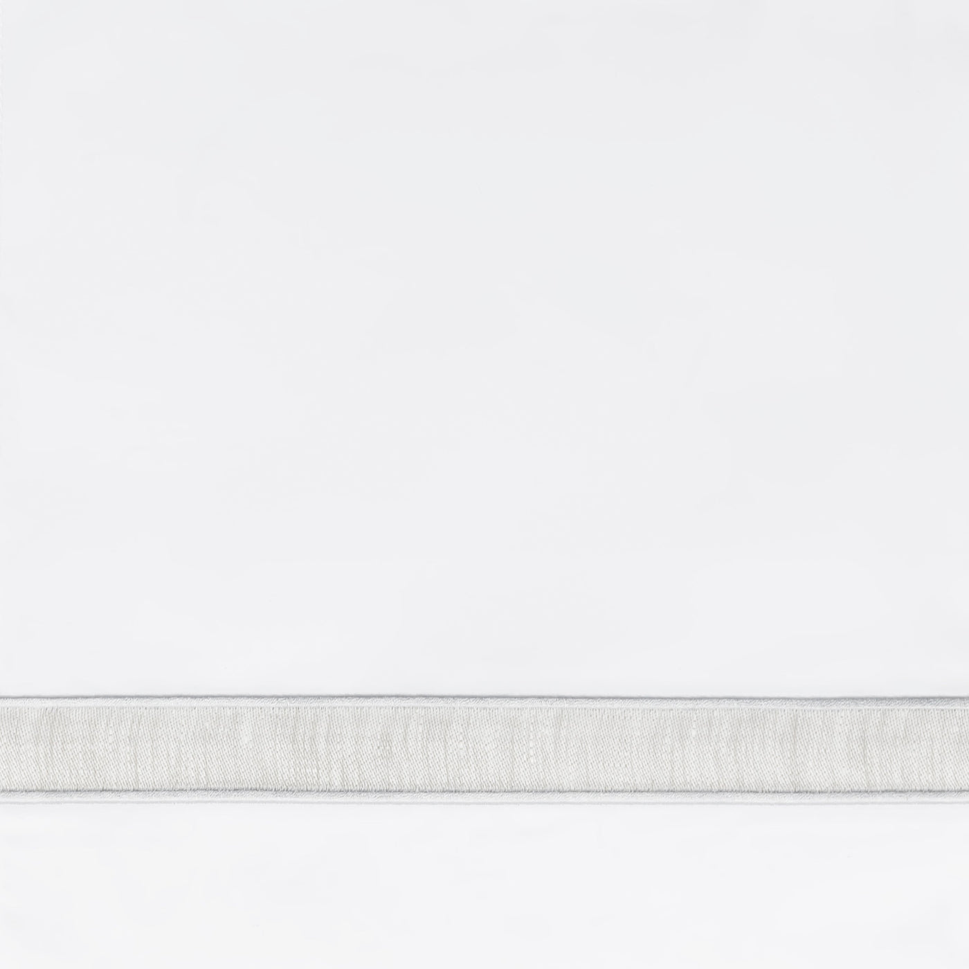 Close-up of white fabric with a narrow woven silver-grey border trim detail.