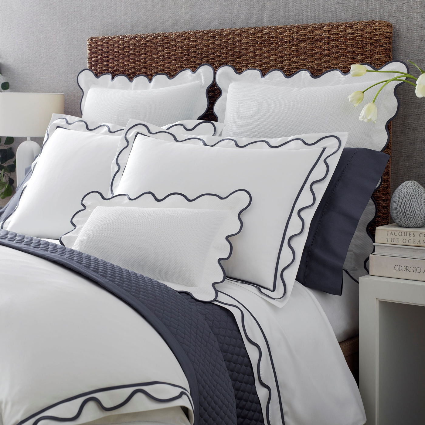 White cotton bedding set with navy scalloped trim, styled on a bed with woven headboard.