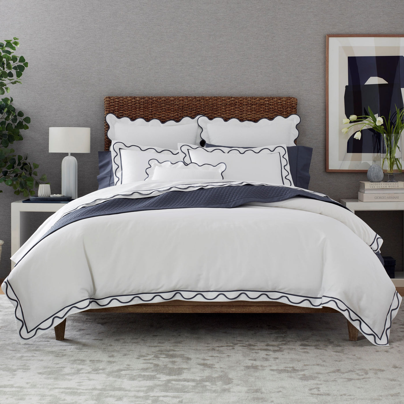 White bedding set with navy scalloped trim on duvet and shams, styled on a rattan bed.