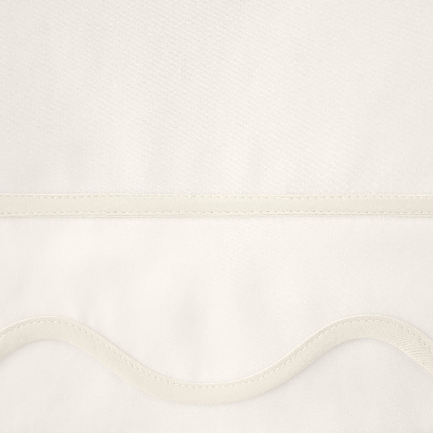 Close-up of ivory fitted sheet hem with scalloped edge and ribbon trim detail.