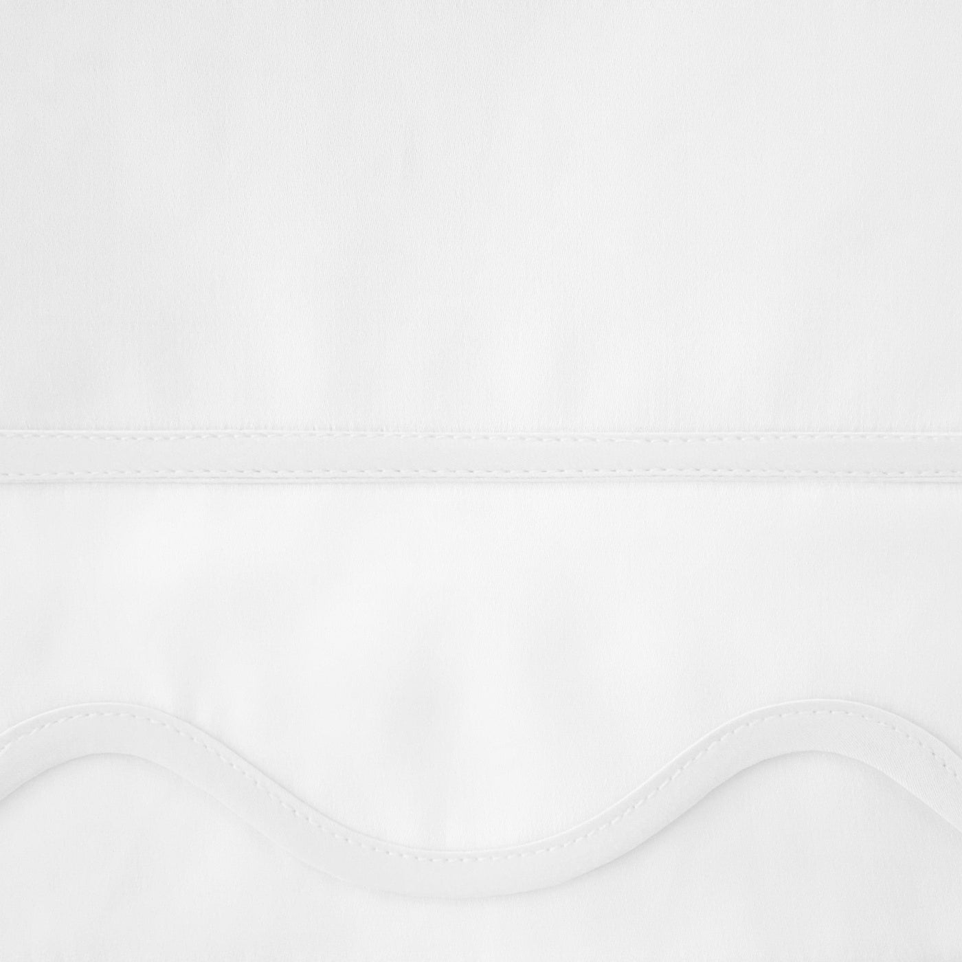 Close-up of white fitted sheet hem with delicate scalloped edge and fine stitching detail.