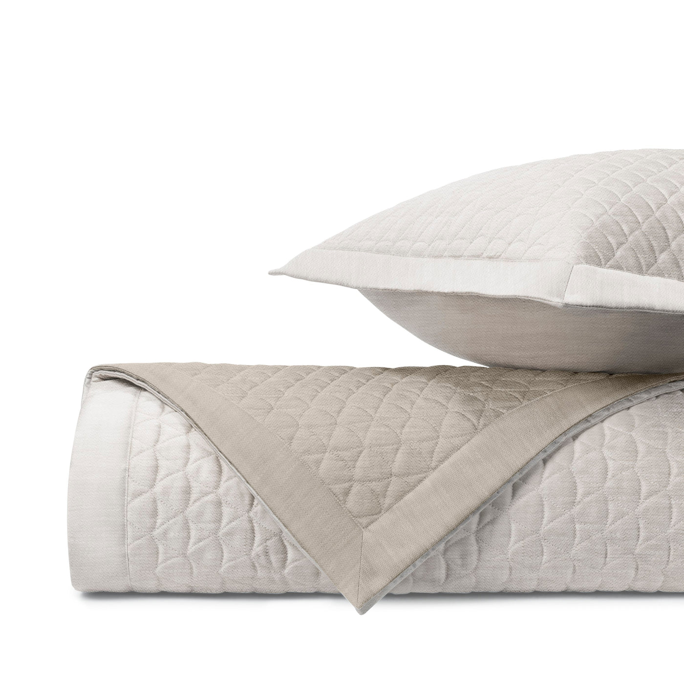 Reverse side of Alina quilted coverlet in taupe, rolled beside matching sham.