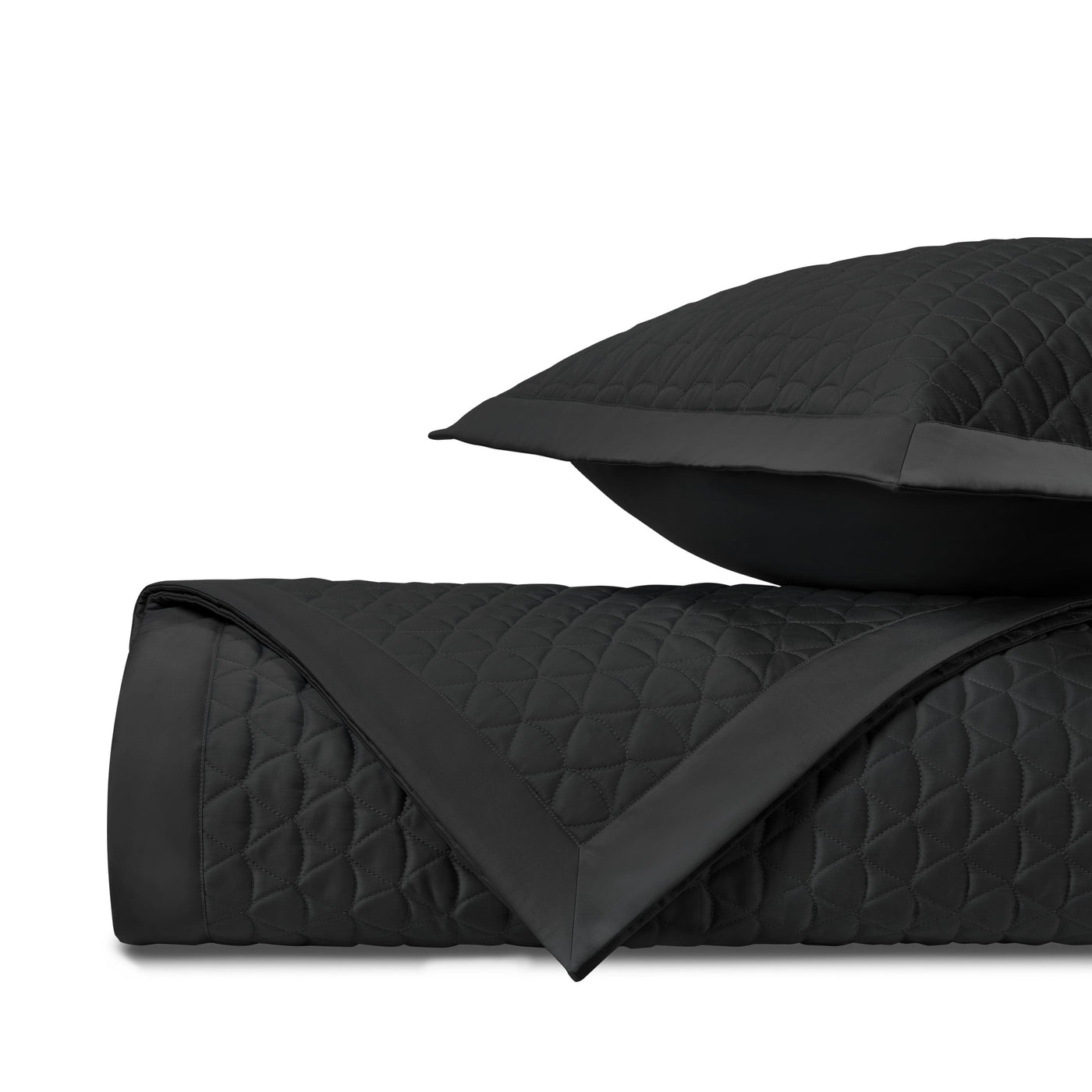 Close-up of black diamond-quilted coverlet with satin trim, folded alongside matching sham.