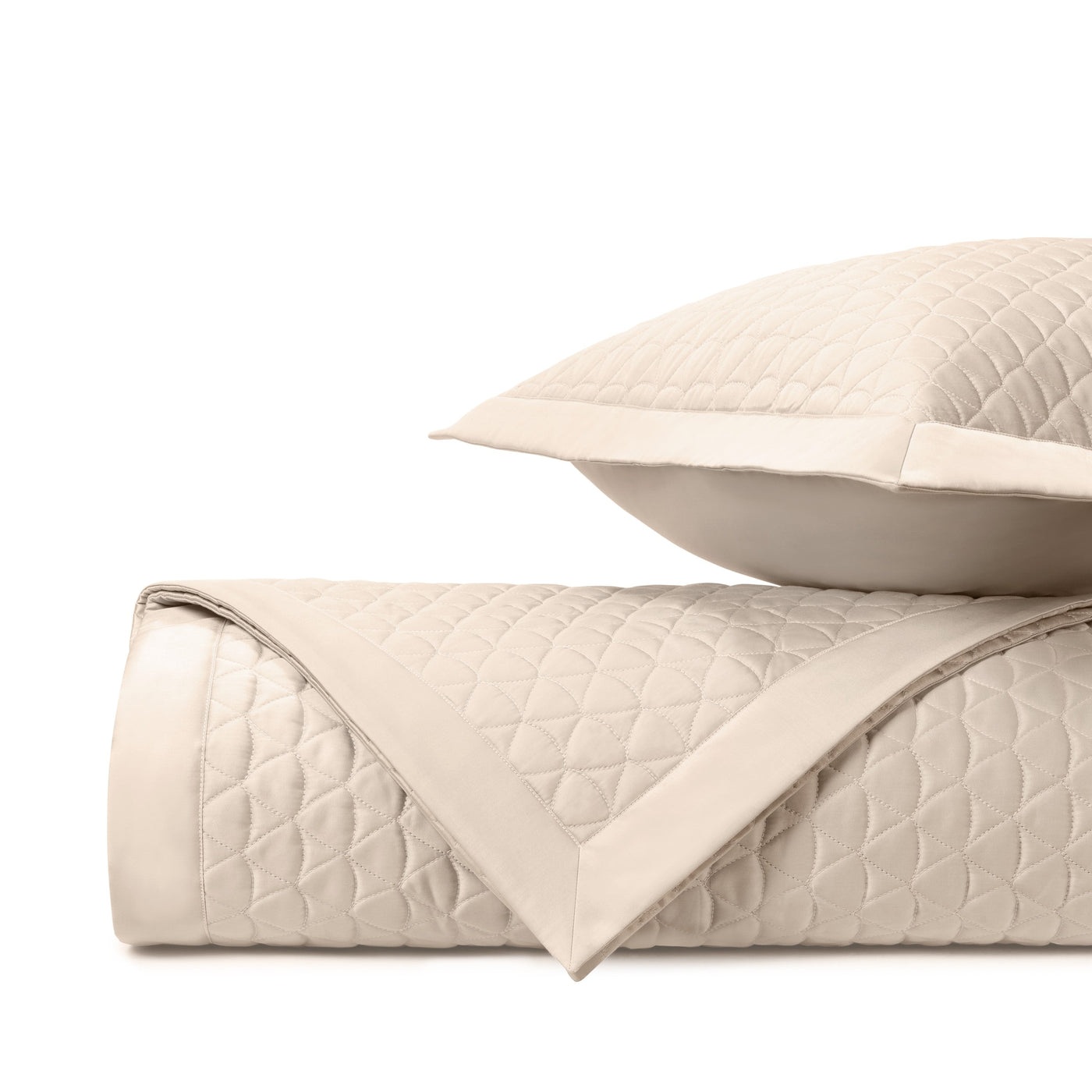 Close-up of ivory quilted coverlet with diamond stitching and satin border, folded with matching sham.