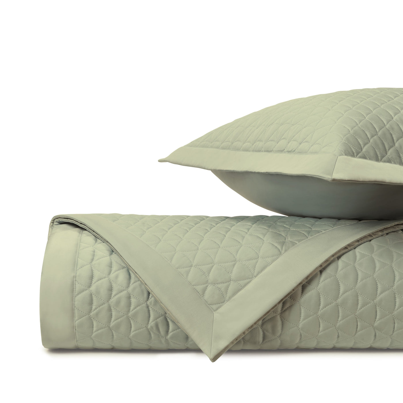 Close-up of sage green quilted diamond-pattern coverlet and sham, rolled and stacked.