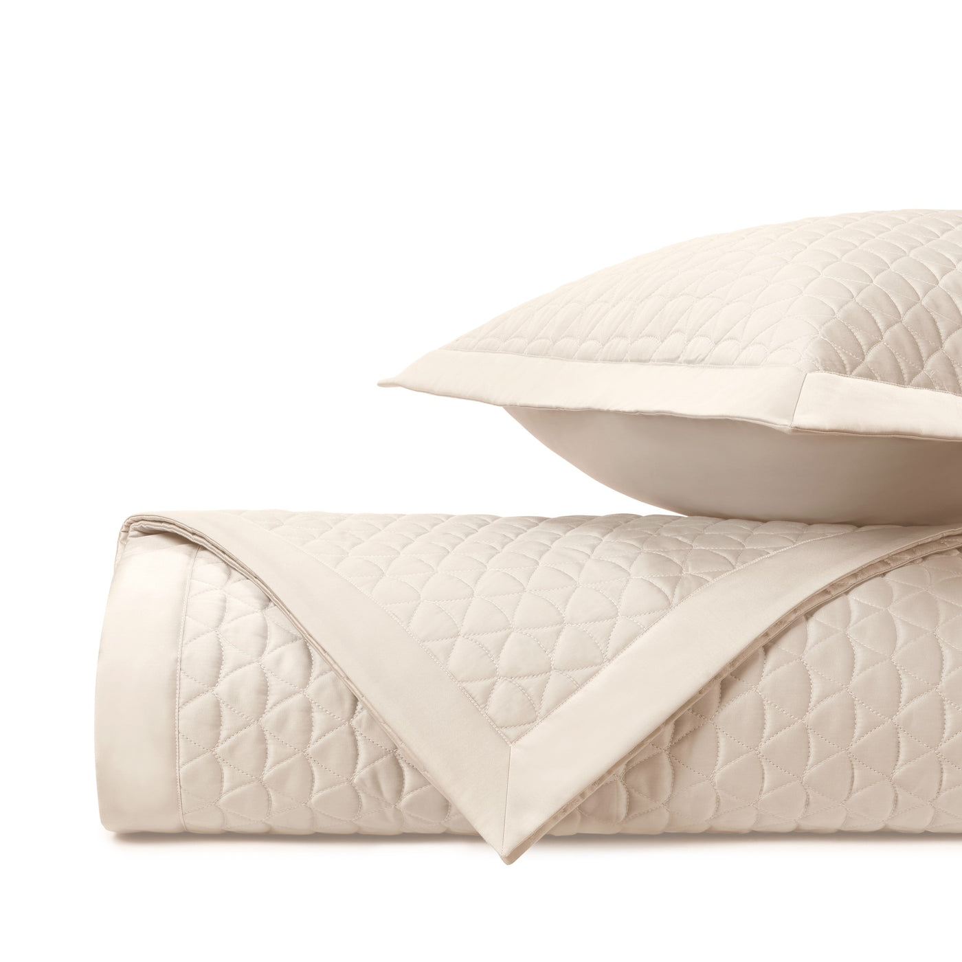 Rolled ivory quilted coverlet with diamond stitching beside a matching sham.