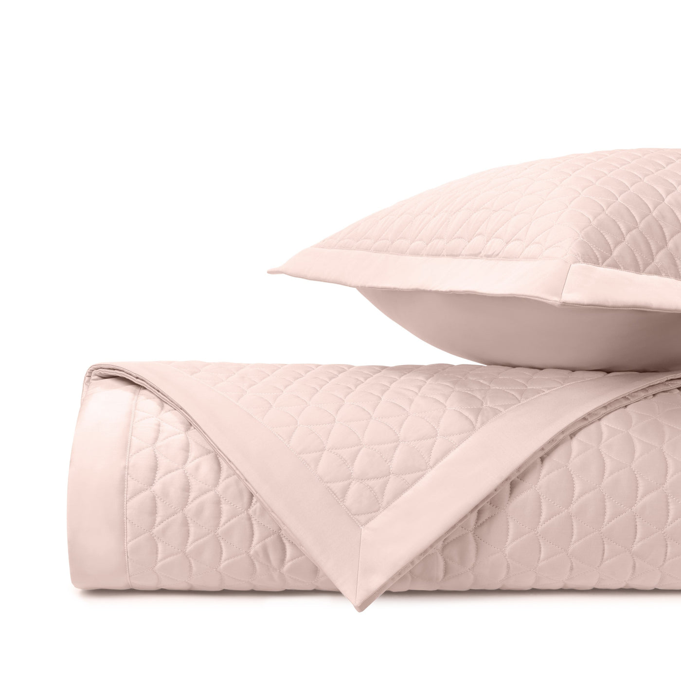 Close-up of blush quilted diamond pattern and satin border on folded coverlet and sham.
