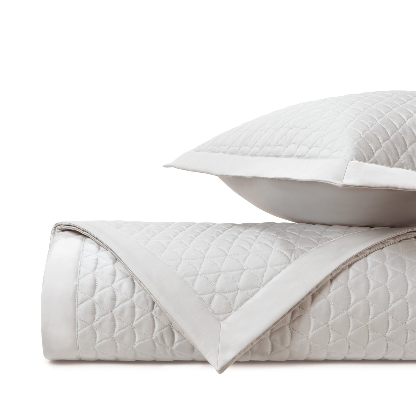 Close-up of ivory diamond-quilted coverlet with white satin border, folded with matching sham.
