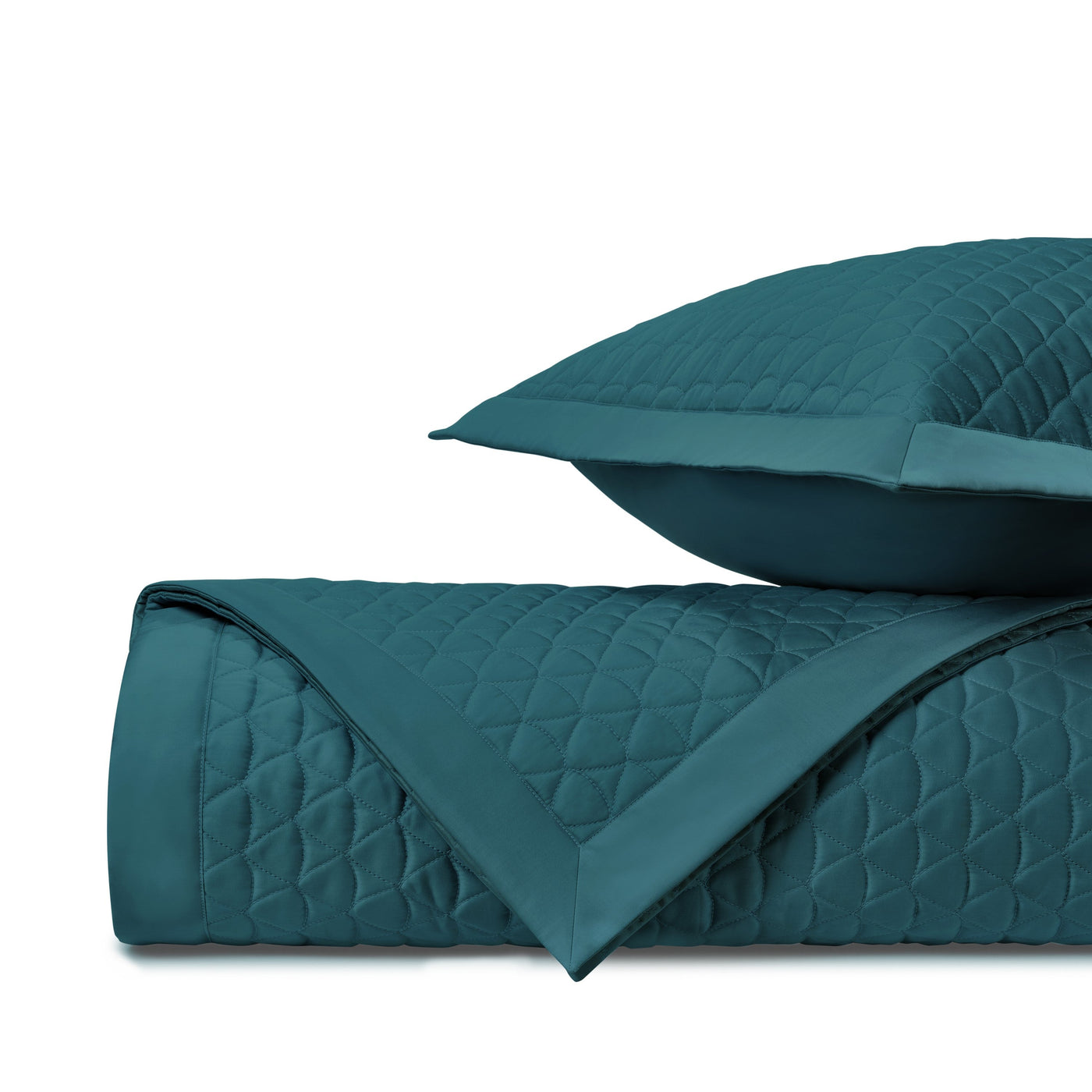 Teal quilted coverlet rolled and stacked with matching sham, diamond stitching detail visible.