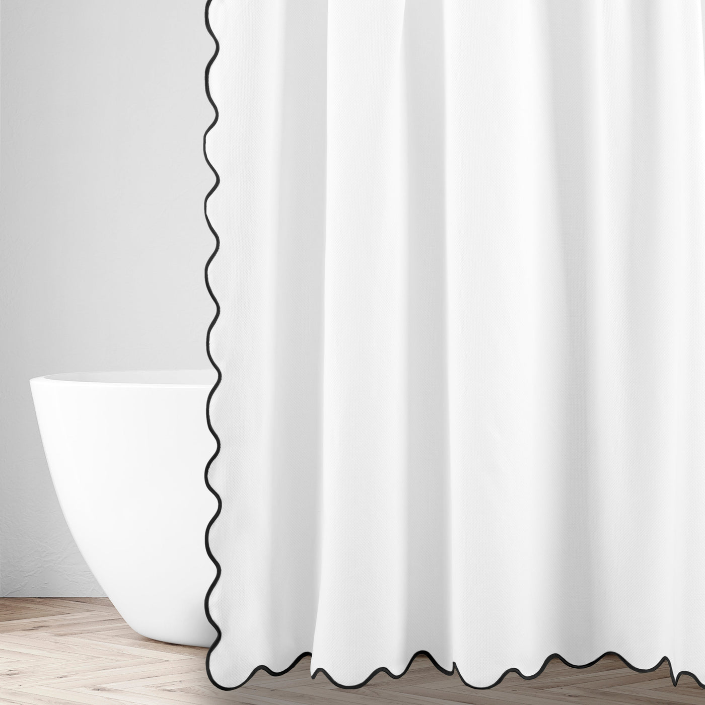 Black scalloped trim detail on white linen shower curtain edge, freestanding tub in background.