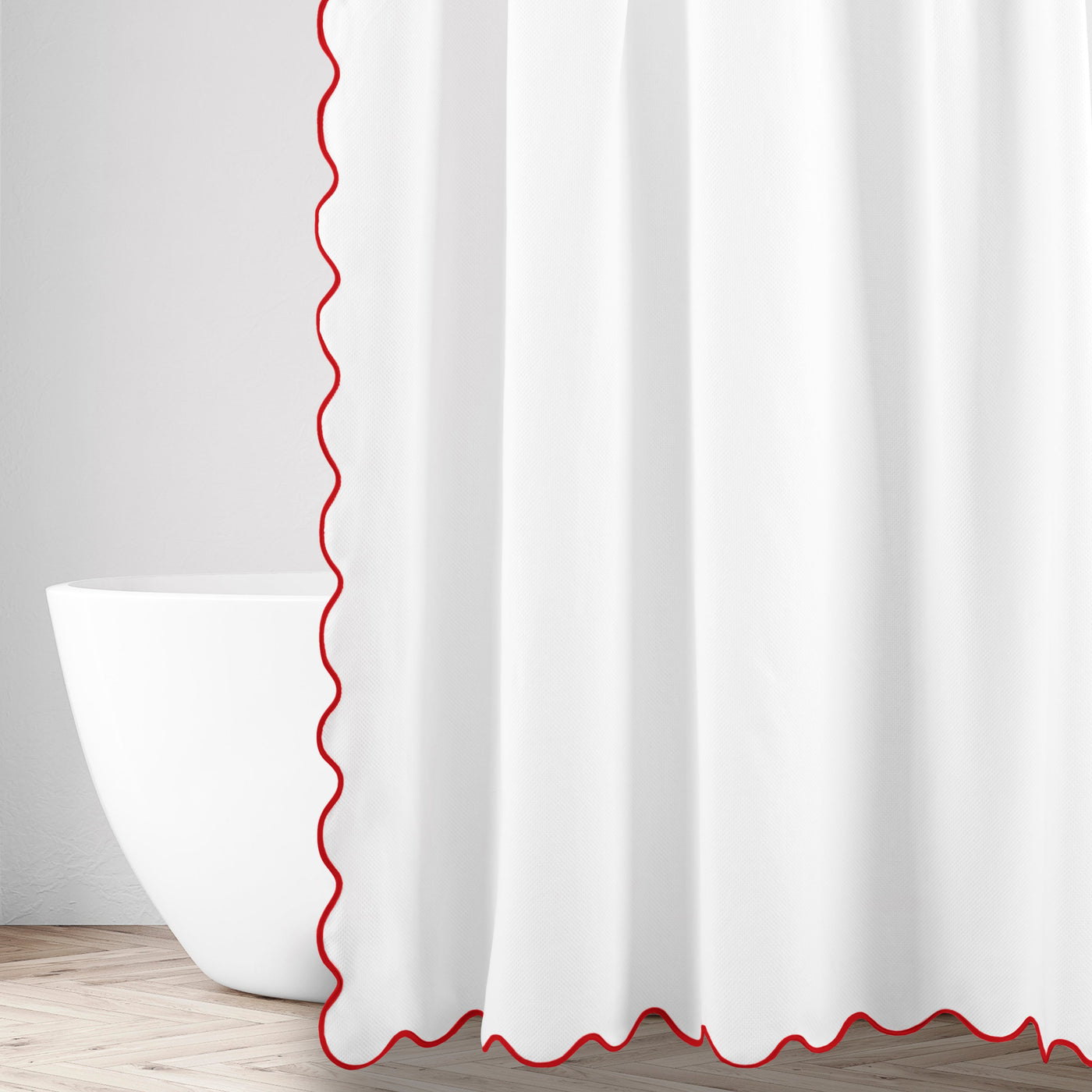 Close-up of white fabric with red scalloped edge trim, draped as shower curtain beside freestanding tub.