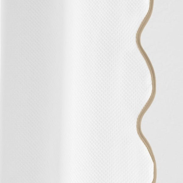 Close-up of white woven fabric with a scalloped champagne border edge.
