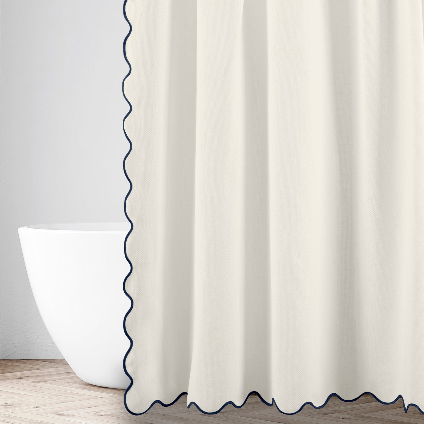 Ivory shower curtain with navy scalloped trim edge, styled in a bathroom with a freestanding tub.