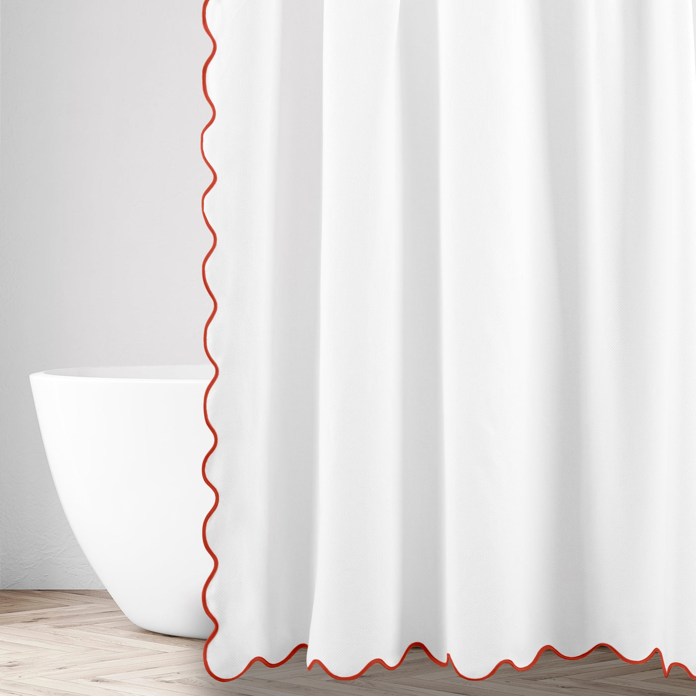 Close-up of white fabric with red scalloped edge trim beside a freestanding bathtub.