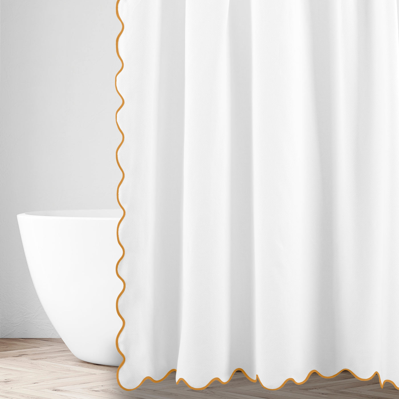 White linen shower curtain with marigold scalloped edge trim, draped beside a freestanding tub.