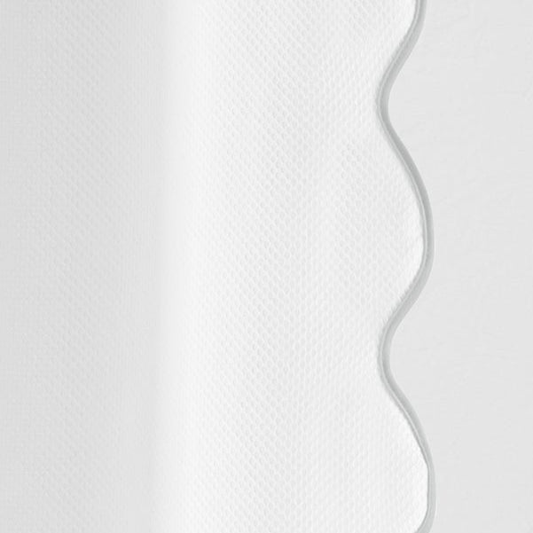 Close-up of white woven fabric with a scalloped wavy edge detail.