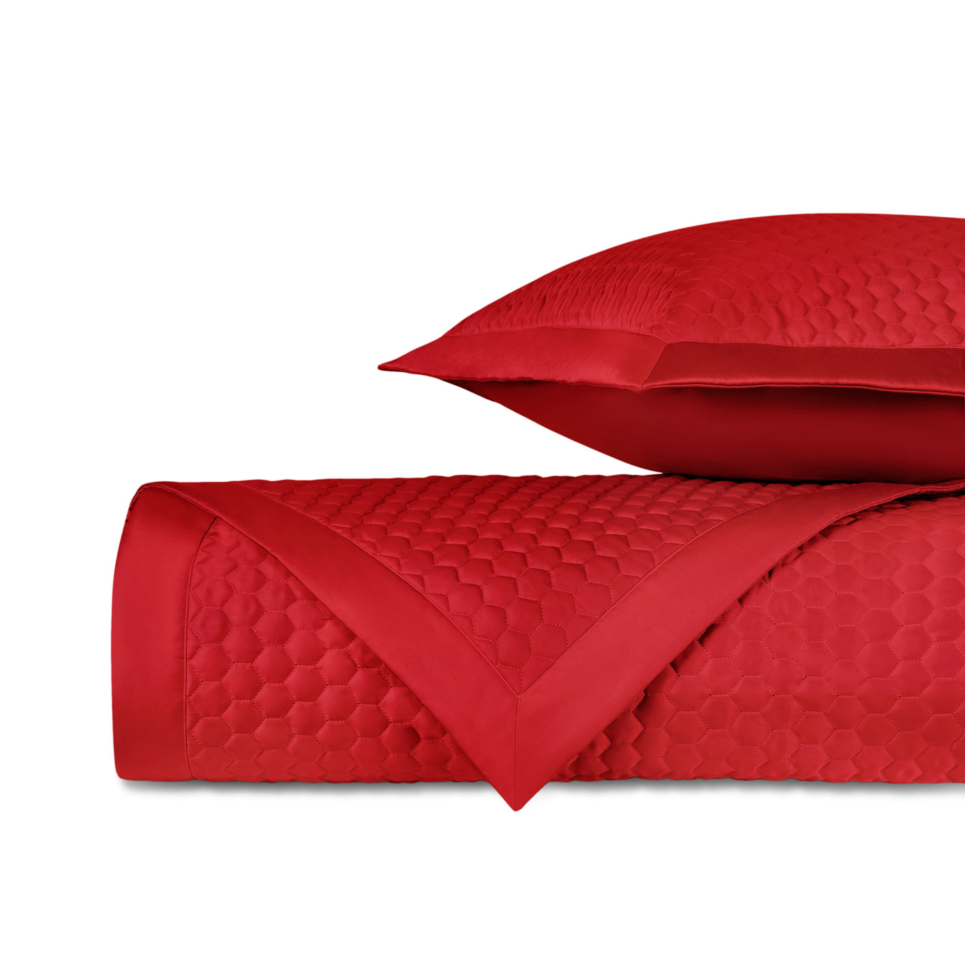 Crimson quilted honeycomb-patterned coverlet rolled beside matching satin-bordered sham.