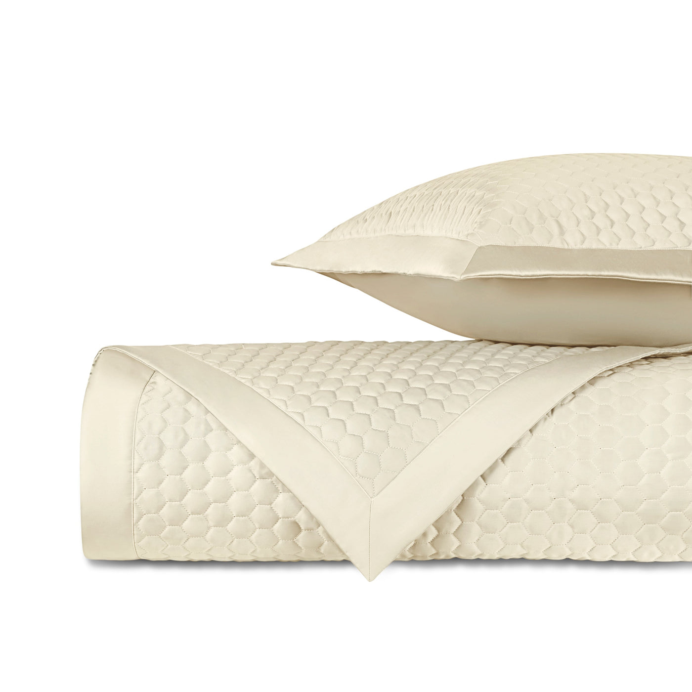Close-up of ivory honeycomb-quilted fabric with satin border trim, shown rolled with matching pillow.