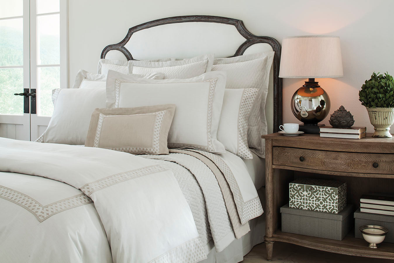 Home Treasures Ara bedding in ivory and taupe styled on a bed with carved wood headboard.