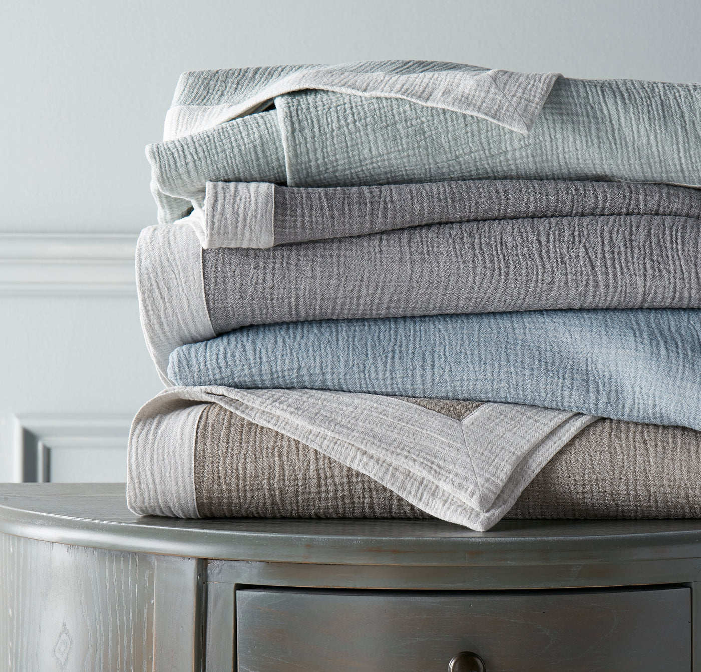 Home Treasures Atacama throws stacked in mist, stone, and ivory on a silver nightstand.
