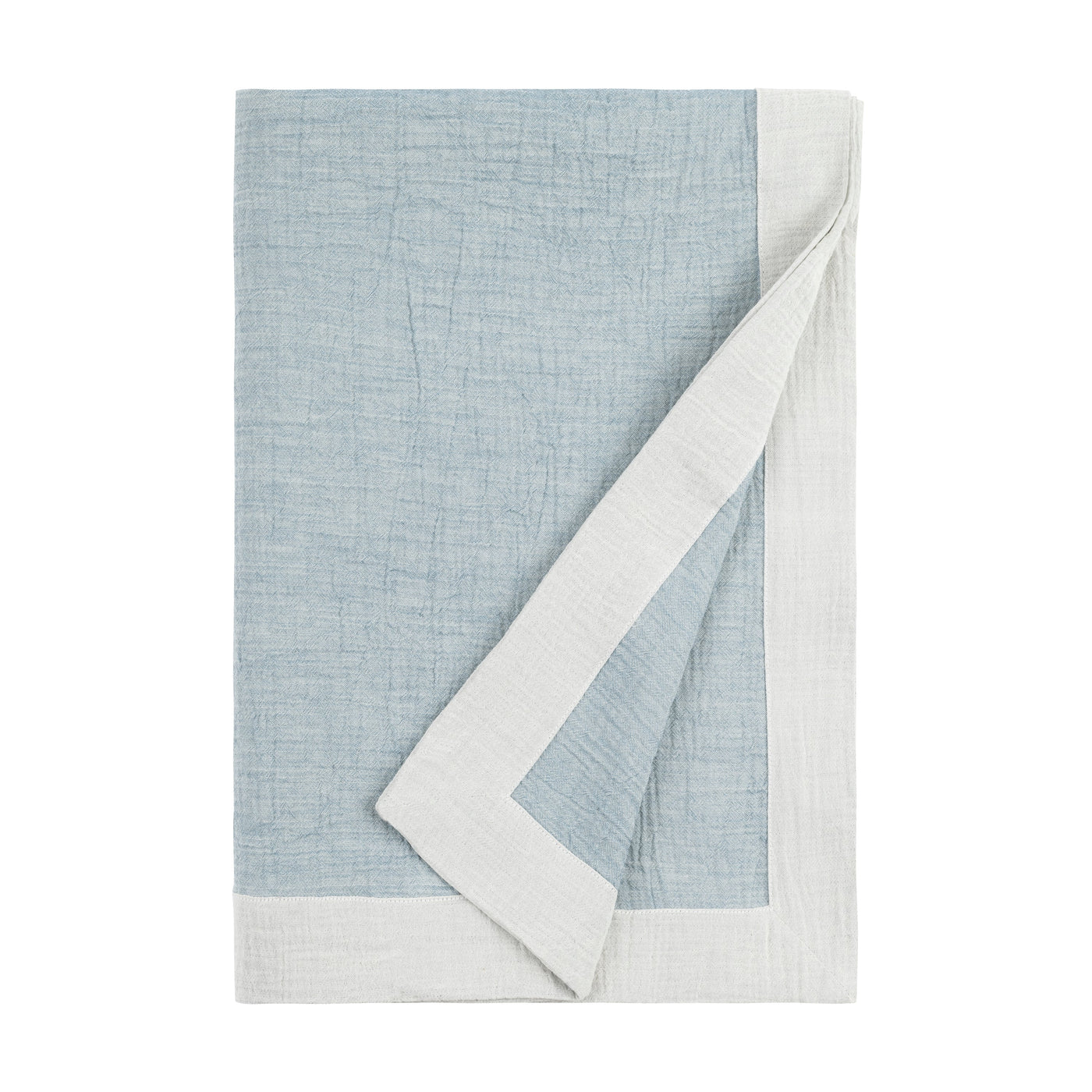 Corner folded back revealing white reverse of a dusty blue linen throw.