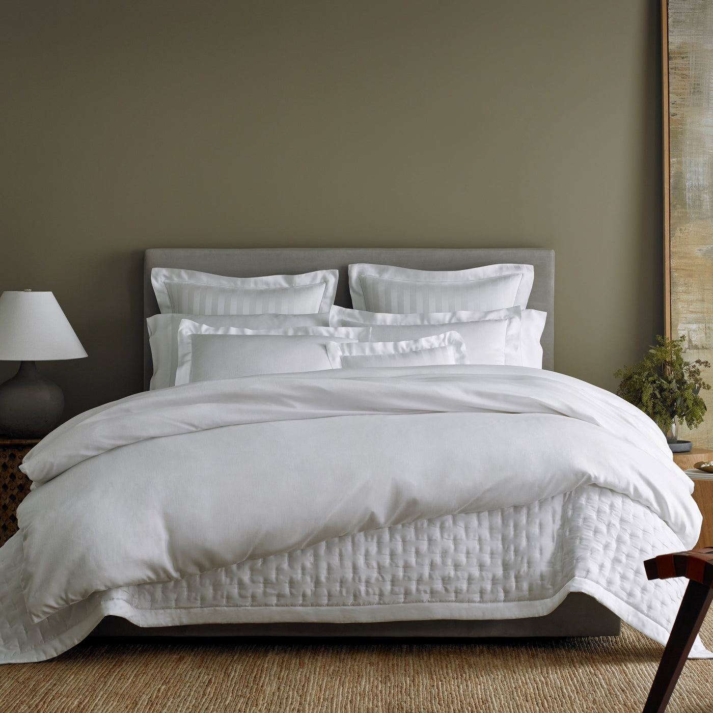 White quilted cotton coverlet and shams styled on a bed in a sage green bedroom.