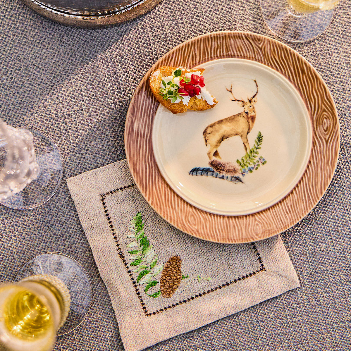 Forest Walk stag cocktail plate with an appetizer on a linen napkin with glasses on a gray table