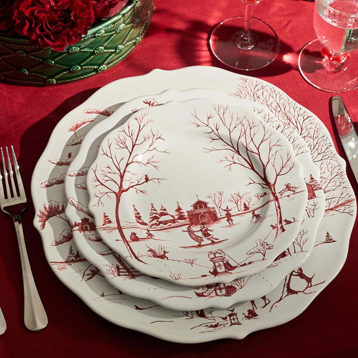 Stacked ruby Winter Frolic charger and plates on a red tablecloth