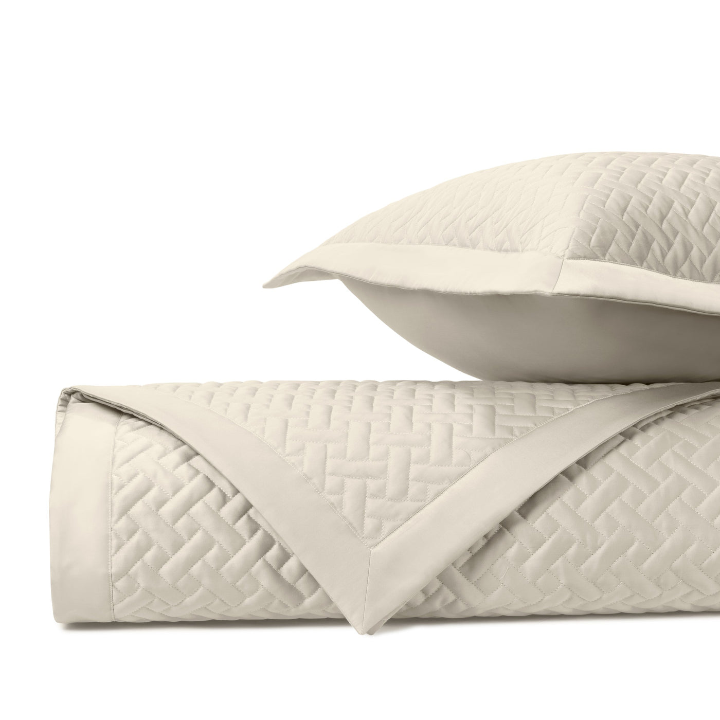 Close-up of ivory quilted basketweave texture with satin trim on folded coverlet and sham.