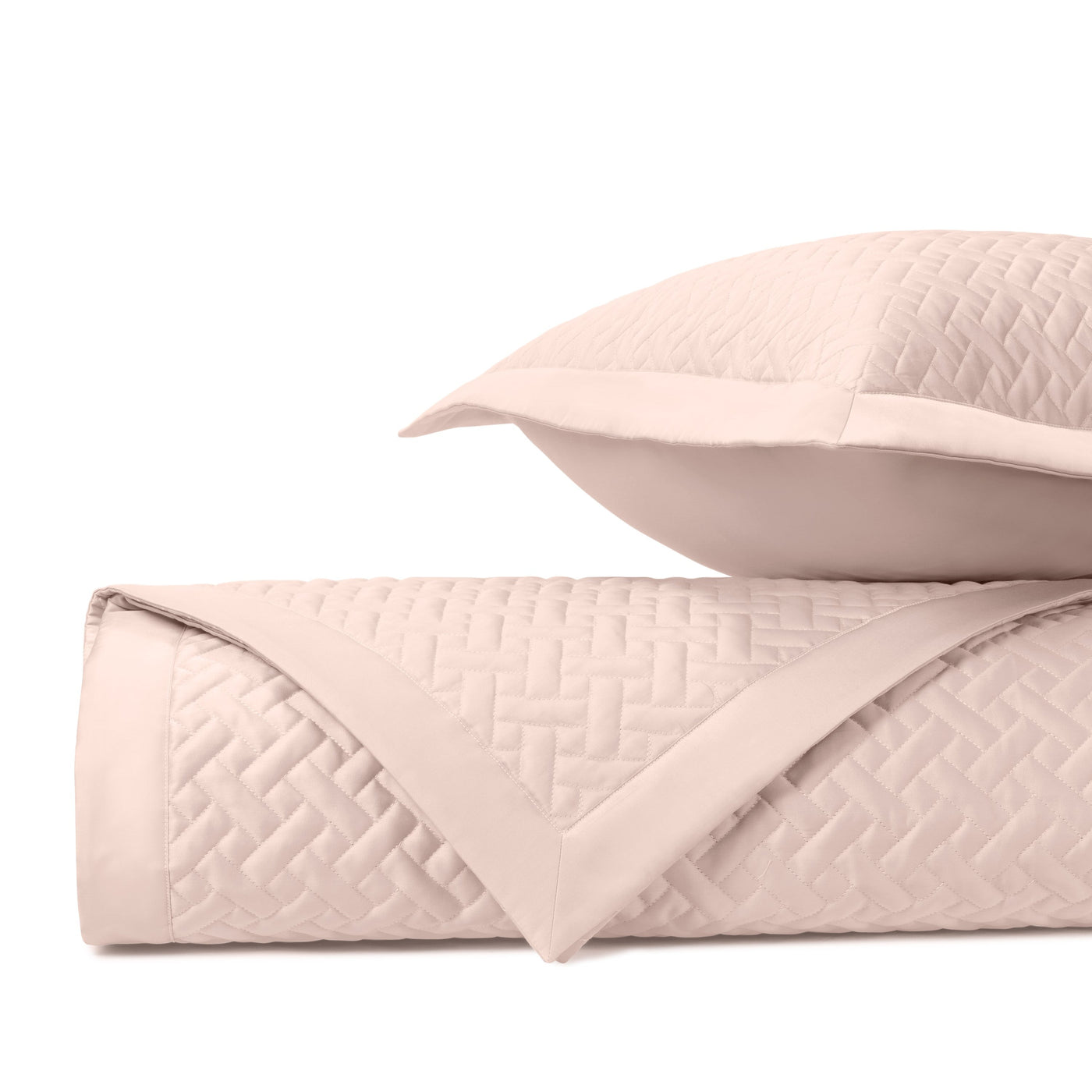 Close-up of blush basketweave quilted texture on folded coverlet and sham.