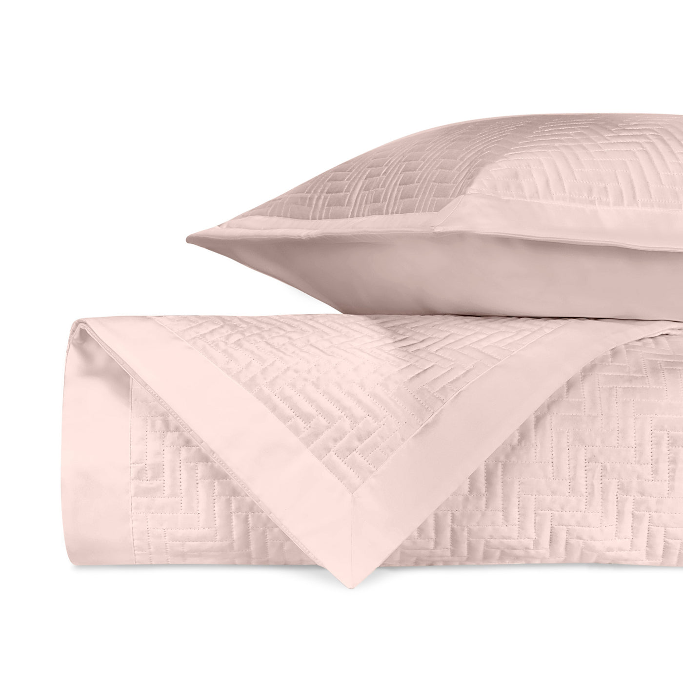 Close-up of blush quilted coverlet with herringbone pattern, folded with matching sham.