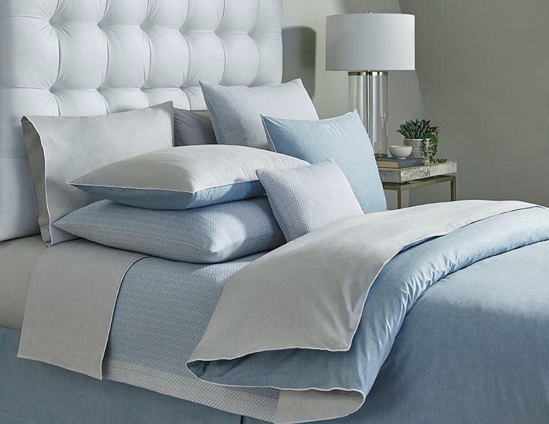 Pale blue and silver grey textured cotton bedding layered on a styled bed.