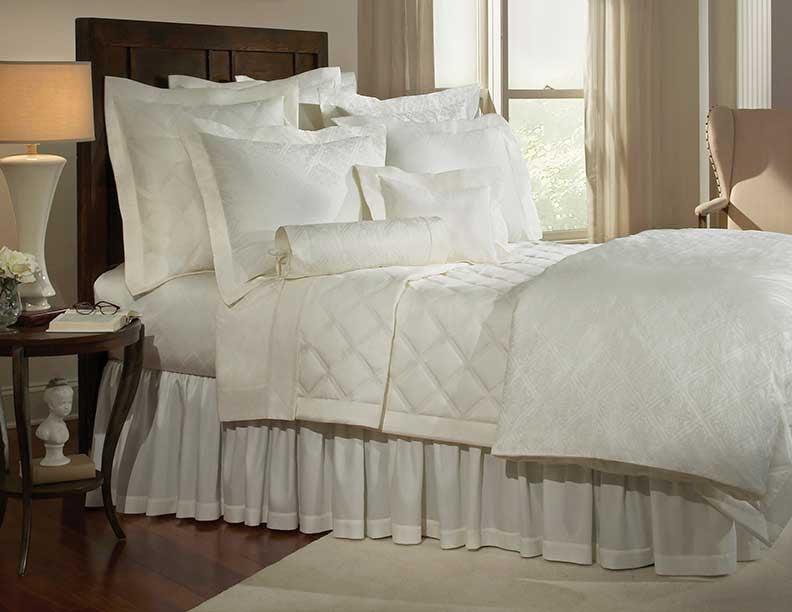 Ivory quilted coverlet and ruffled bed skirt styled on a dressed bed.