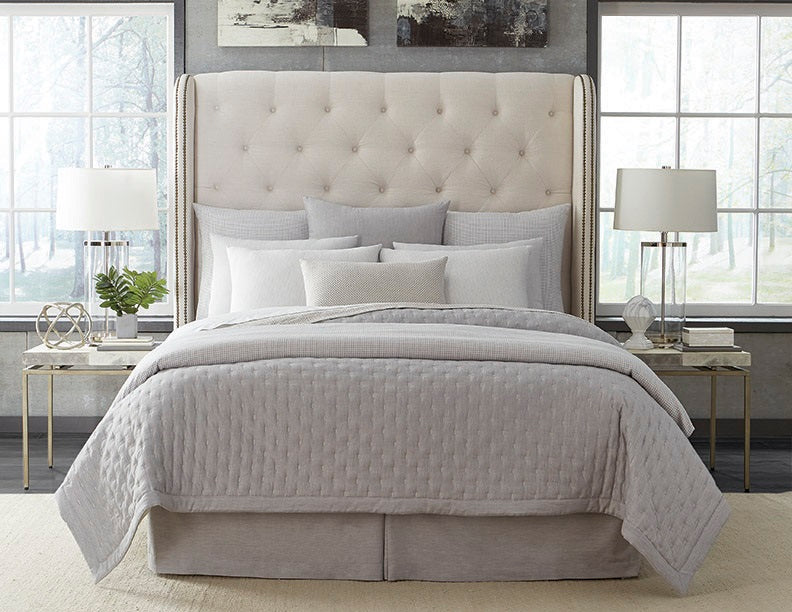 Dove grey quilted coverlet styled on a made bed with layered ivory and silver pillows.